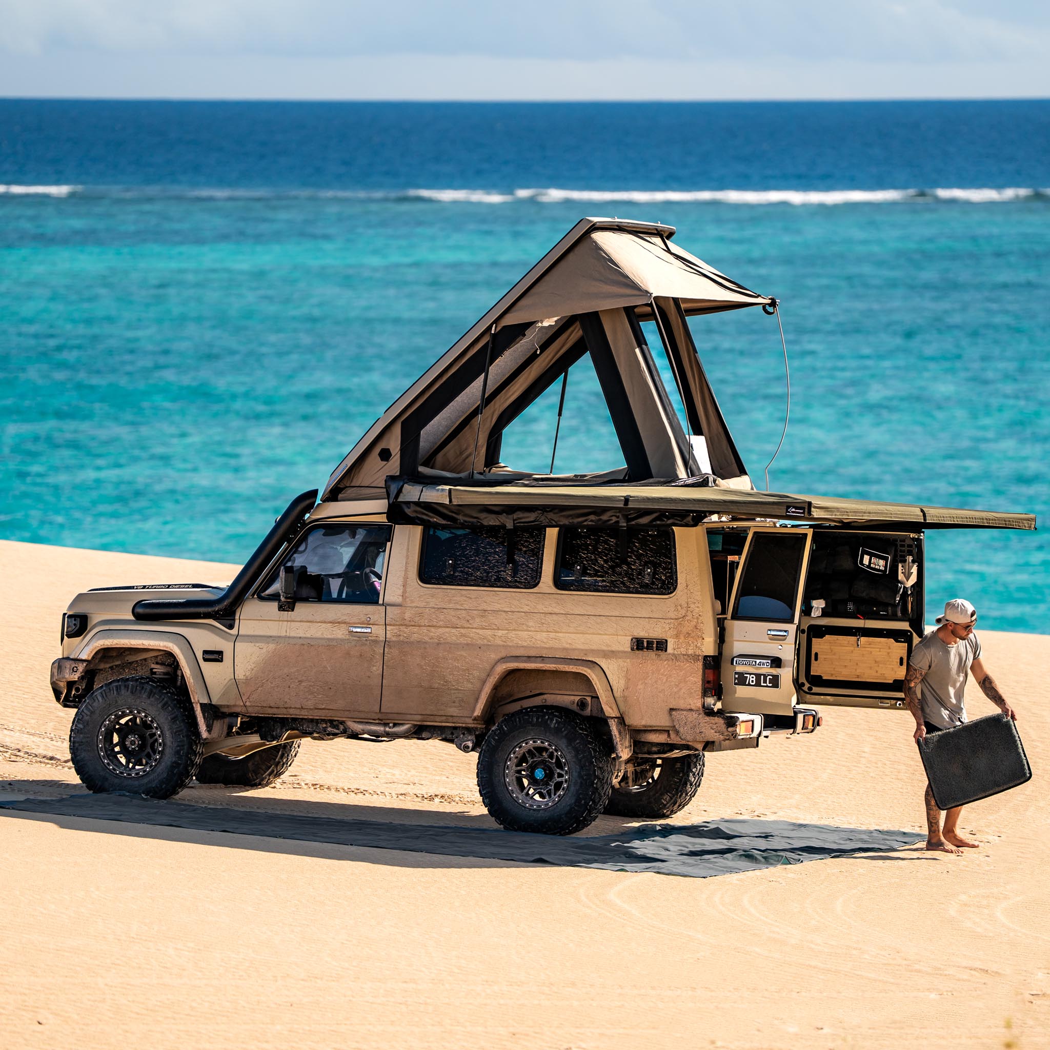 Camping setup with chairs, table, and a vehicle overlooking a scenic, green landscape.