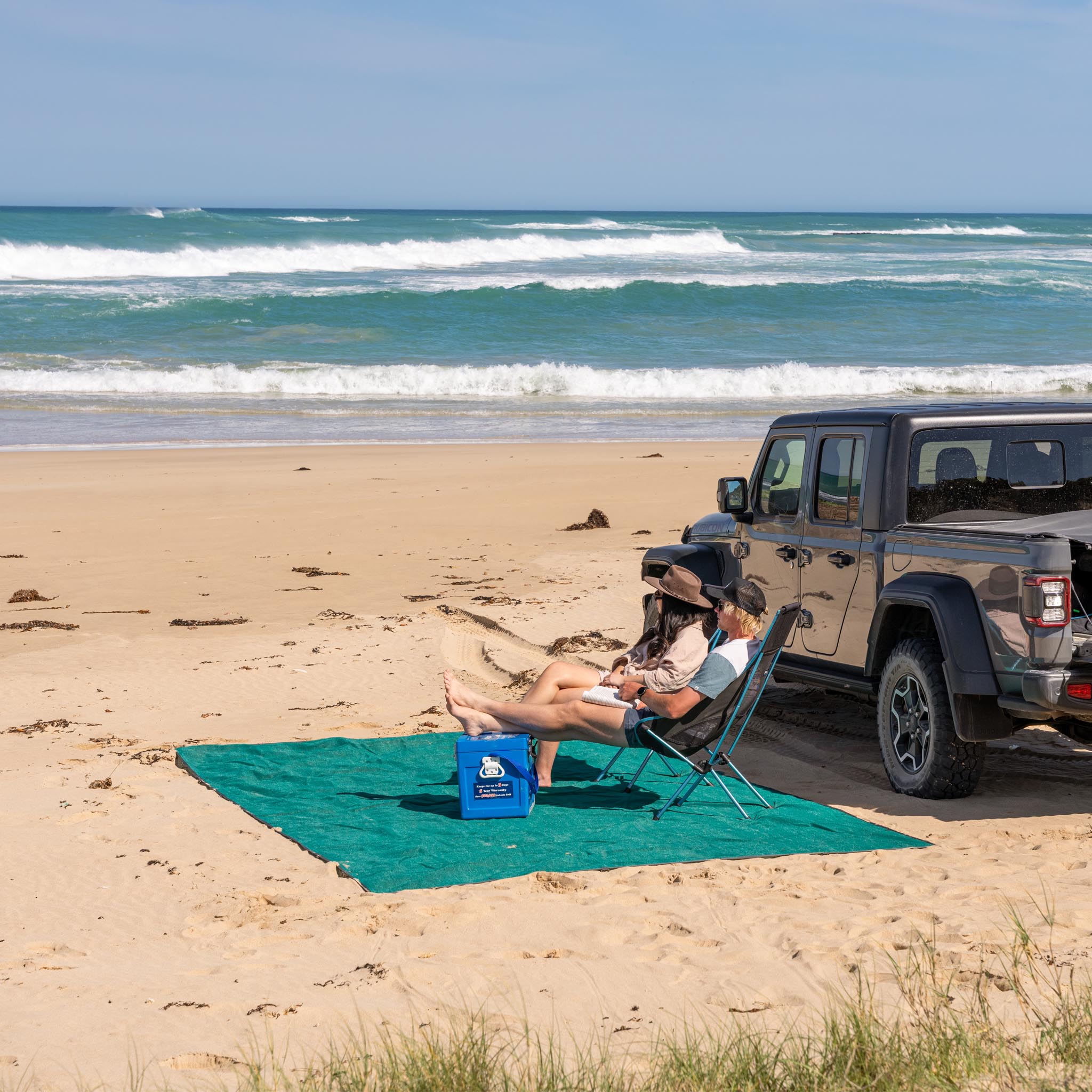 Camping setup with chairs, table, and a vehicle overlooking a scenic, green landscape.