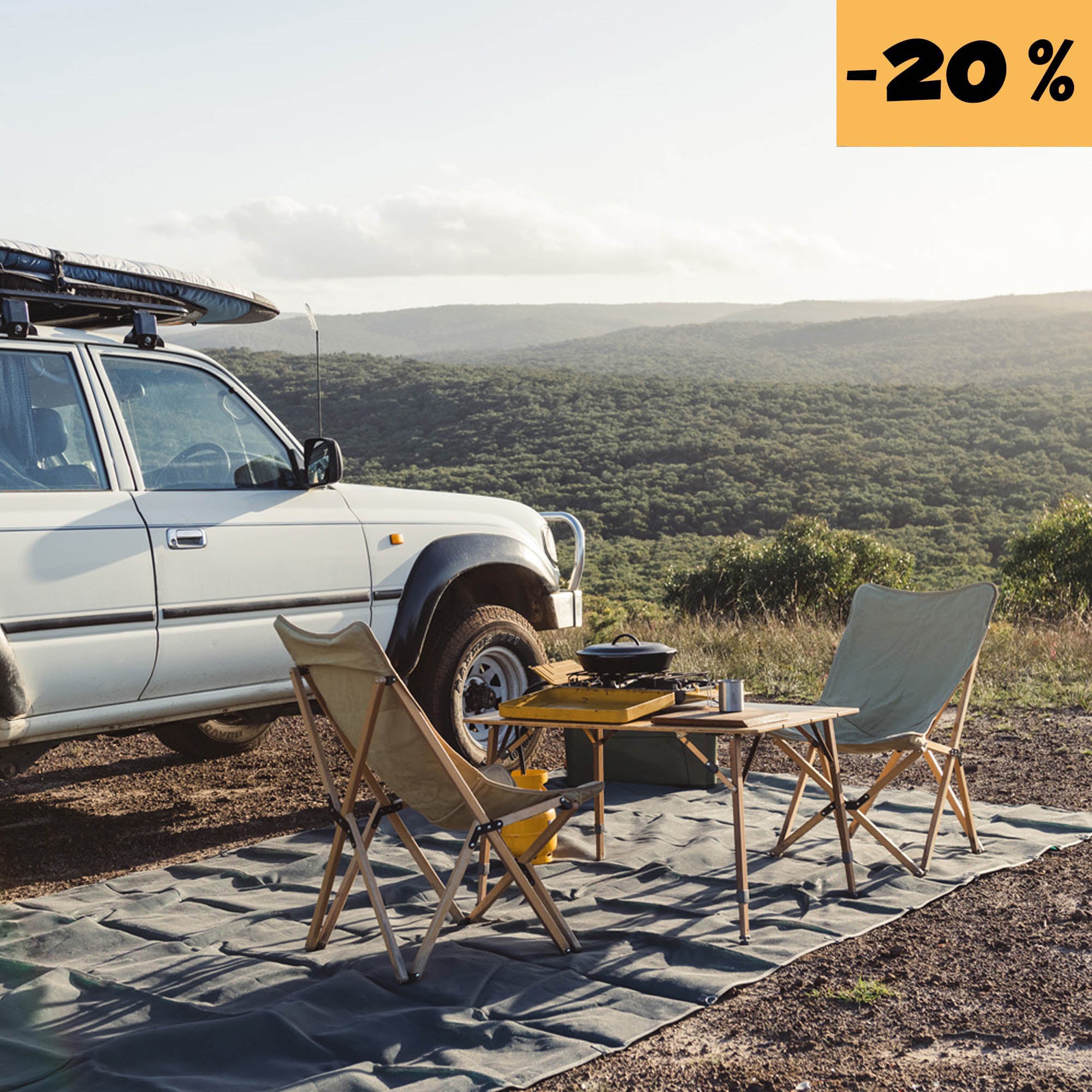 Camping setup with chairs, table, and a vehicle overlooking a scenic, green landscape.